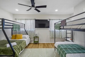 Ein Zimmer mit Etagenbetten, einem Deckenventilator, einem Fernseher und einem kleinen Tisch mit Lampe.