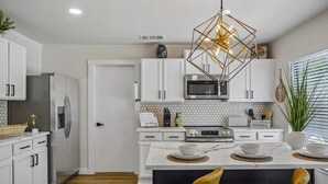 A modern kitchen with white cabinetry, a stainless steel refrigerator, a microwave, and a dining area with a marble countertop and two chairs. - Spacious 4BR San Antonio Home w/ Private Pool, Game Rooms & Gym (San Antonio)