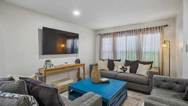 A modern living room with a flat-screen TV, grey sofas, a blue coffee table, and a wooden side table. - Spacious 4BR San Antonio Home w/ Private Pool, Game Rooms & Gym (San Antonio)