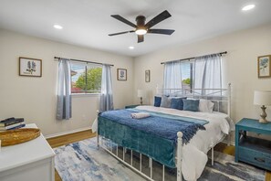 Ein Schlafzimmer mit einem Bett, einem Deckenventilator, einem Fenster mit Vorhängen und einem Nachttisch.