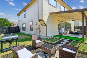 Ein Haus mit überdachter Terrasse, Gartenmöbeln, Grill und gepflegtem Rasen.