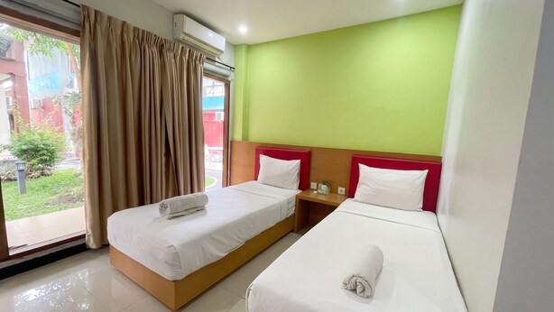 A hotel room with two beds, a window with curtains, a nightstand, and a green wall.