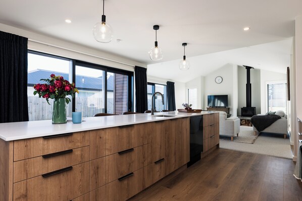 A modern kitchen with a large island, wooden cabinets, and pendant lighting.