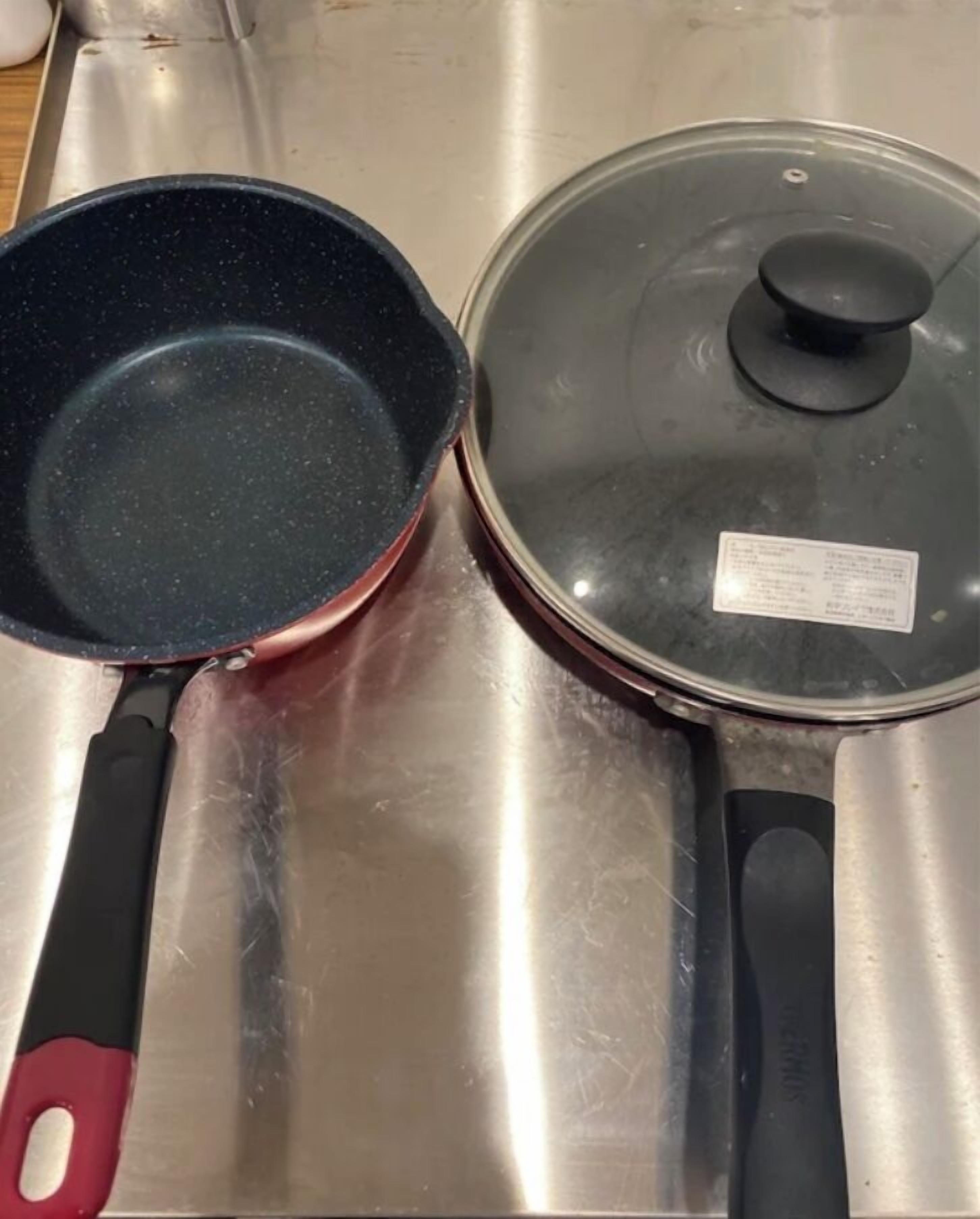 A stainless steel kitchen counter with a frying pan and a pot with a lid.