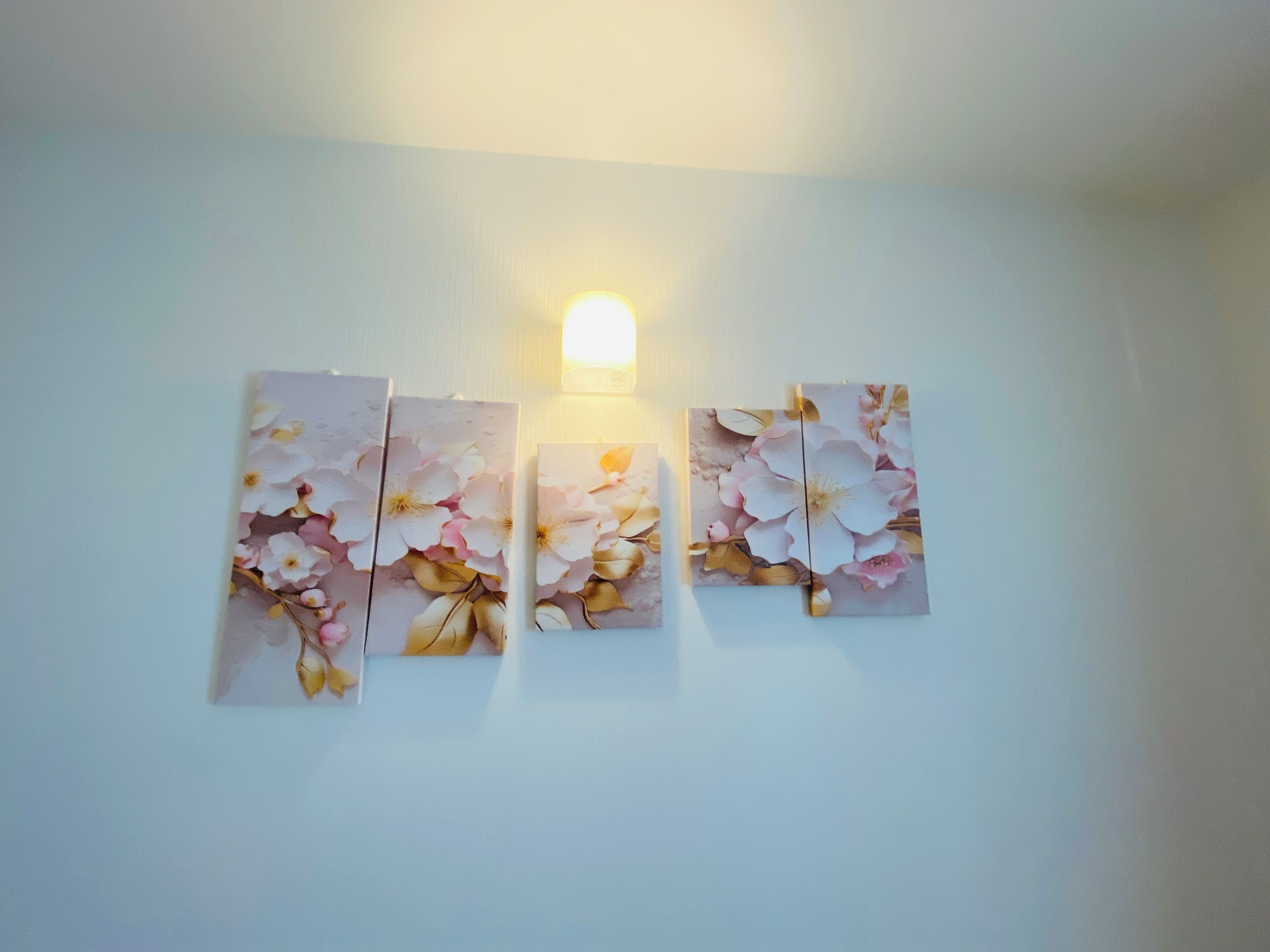 A wall with three floral paintings and a wall-mounted light fixture.