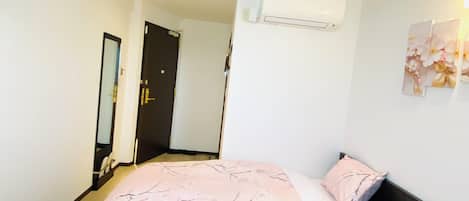 A bedroom with a bed, a bedside table, a wall-mounted air conditioner, and a door.