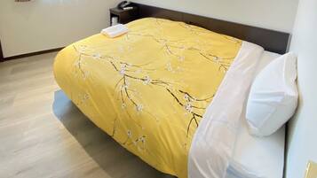 A hotel room with a bed, a nightstand, a window with curtains, a wall-mounted air conditioner, and a ceiling light.