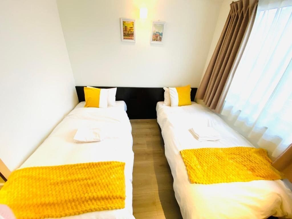 A hotel room with two beds, each with a yellow blanket, a black headboard, and a small table between them.