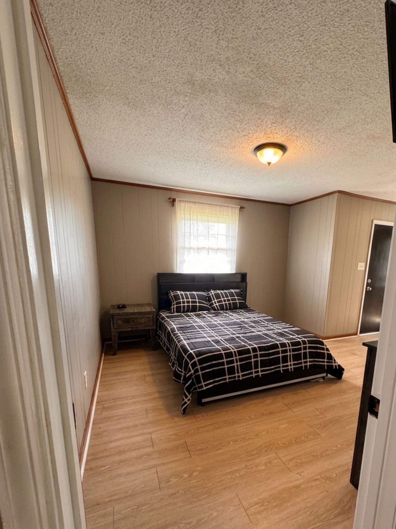 A bedroom with a bed, a nightstand, a window with curtains, and a door.