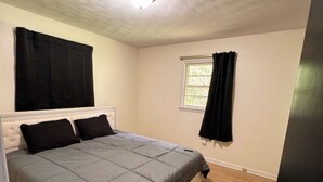 Een slaapkamer met een bed, een raam met gordijnen, een deur en een plafond met een lamp.