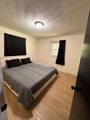 A bedroom with a bed, a window with curtains, a door, and a ceiling with a light fixture. - Soothing 3-bedroom house with AC in charming Gaffney (Gaffney)