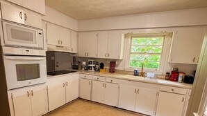 Een praktische keuken met witte kastjes, een magnetron, een oven, een spoelbak en een raam met uitzicht op groen.