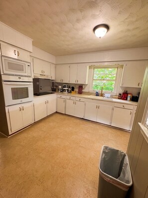 A compact kitchen with white cabinets, a microwave, an oven, a sink, and a window with a view of greenery. - Soothing 3-bedroom house with AC in charming Gaffney (Gaffney)