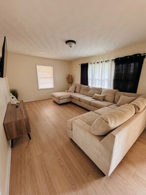 A living room with a beige sectional sofa, a wooden coffee table, a small plant, and a window with blinds. - Soothing 3-bedroom house with AC in charming Gaffney (Gaffney)