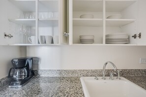 A kitchen with a granite countertop, a coffee maker, a sink with a faucet, and cabinets with glassware and plates. - Blueground | Upper West Side, rooftop, nr Central Park (New York)