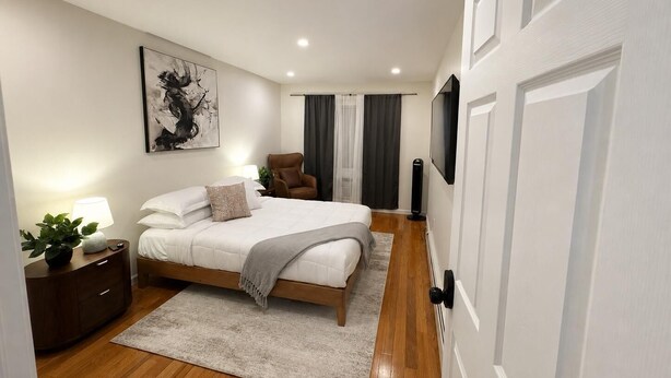 Ein modernes Schlafzimmer mit einem großen Bett, einem Sessel, einem Fernseher und einem Bild an der Wand.