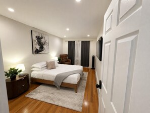 A modern bedroom with a large bed, a chair, a TV, and a painting on the wall. - The Bed-Stuy Cozy Room + Suite • Near Fulton St (Brooklyn)