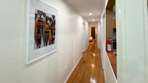 Ein Flur mit einem gerahmten, abstrakten Kunstwerk an der Wand, einem Holzboden und einem an der Wand befestigten Feuerlöscher.