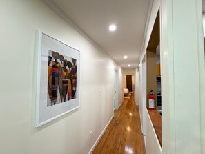 Ein Flur mit einem gerahmten, abstrakten Kunstwerk an der Wand, einem Holzboden und einem an der Wand befestigten Feuerlöscher.