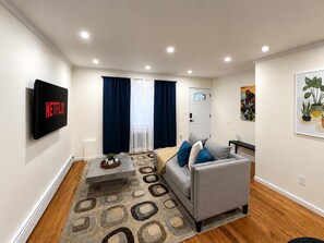 Ein modernes Wohnzimmer mit einem grauen Sofa, einem flachbildfernseher an der Wand und einem gemusterten Teppich.