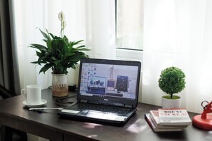 Un ordinador portàtil sobre una taula, amb una tassa, una planta, un arbre petit i llibres.