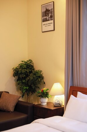 Habitació d'hotel amb un llit, una tauleta de nit amb una làmpada, una planta en test, un sofà i un quadre a la paret.