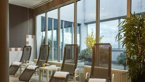 Een wellnessruimte met ligstoelen, een tafeltje met fles en glas, en grote ramen met uitzicht op buiten.