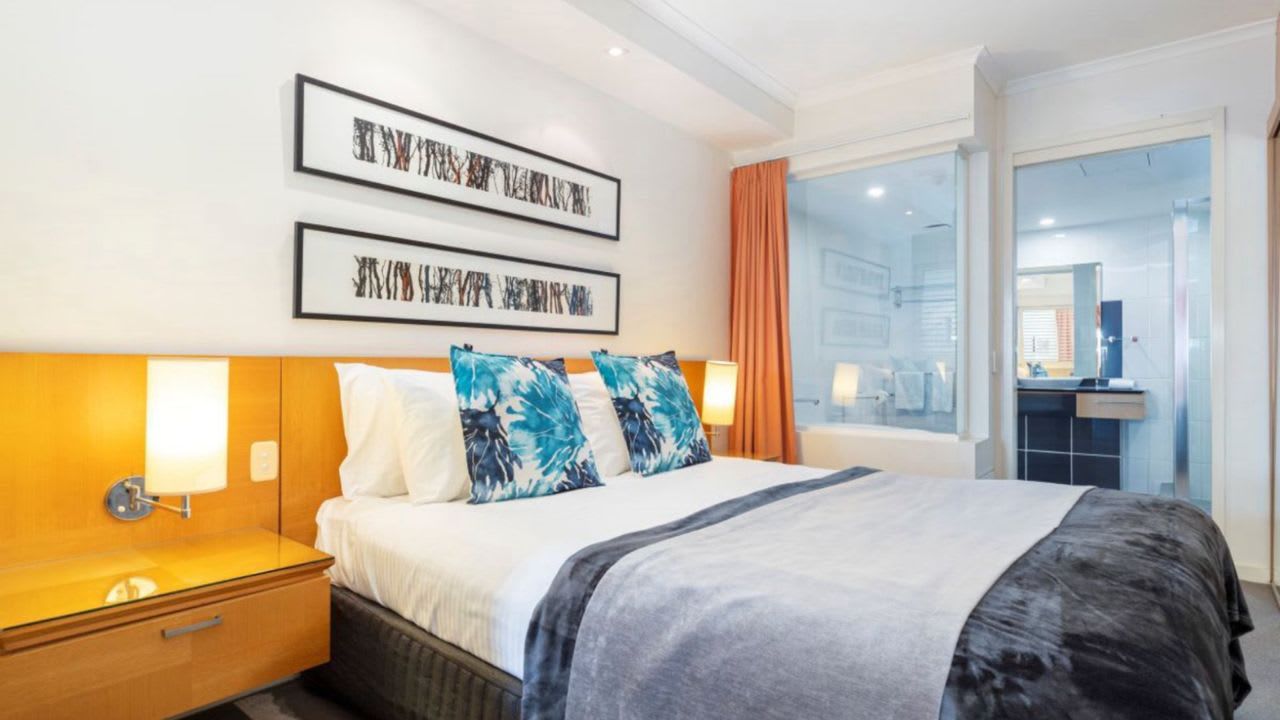 A hotel room with a bed, bedside table, wall art, and a view through a glass door.