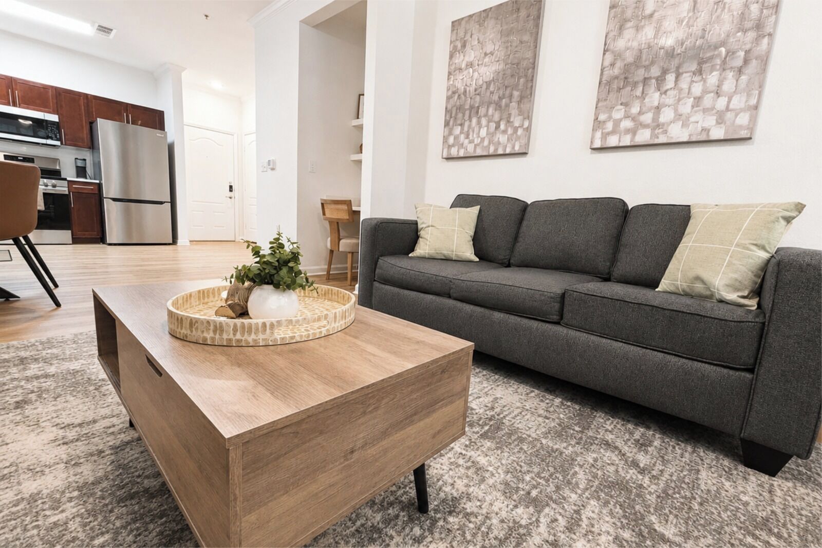 Een moderne woonkamer met een grijze bank, een houten salontafel en abstracte wanddecoratie.