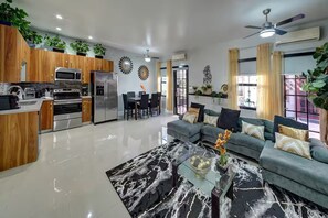 Une cuisine moderne dotée d’appareils électroménagers intégrés, un coin repas avec une table et des chaises, un salon avec un canapé et un ventilateur de plafond.