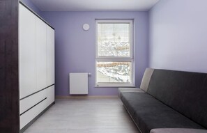 A room with a sofa, a wardrobe, a radiator, and a window with blinds. - Verdant Haven Apartment (Gdańsk)