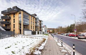 A modern apartment building with balconies, a paved sidewalk, and a road with parked cars. - Verdant Haven Apartment (Gdańsk)
