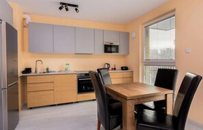 A modern kitchen with grey cabinets, a wooden dining table, and black chairs. - Verdant Haven Apartment (Gdańsk)