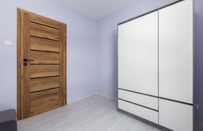 A room with a wooden door, a white wardrobe, and light-colored walls. - Verdant Haven Apartment (Gdańsk)