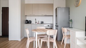 A modern kitchen with white cabinets, a stainless steel refrigerator, a wooden dining table with chairs, and a small countertop with a lamp. - Aleja Krakowska Lavish Apartment (Warszawa)