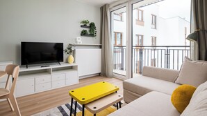 A modern living room with a flat-screen TV, a sofa, a yellow table, and a balcony with a view of buildings. - Aleja Krakowska Lavish Apartment (Warszawa)