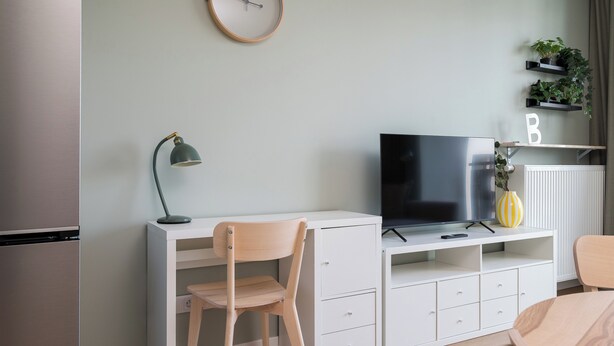 A modern living room with a flat-screen TV, a desk, a chair, a lamp, and a radiator. - Aleja Krakowska Lavish Apartment (Warszawa)
