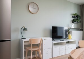 Ein modernes Wohnzimmer mit Flachbildfernseher, Schreibtisch, Stuhl, Lampe und Heizkörper.