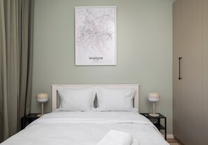 Ein Schlafzimmer mit einem Bett, zwei Nachttischen, einer an der Wand befestigten Karte von Warschau, Polen, und einem Vorhang.