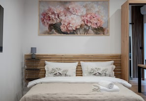 A neatly made bed with floral pillows, a wooden headboard, and a painting of flowers above it. - Heart of Cracow Cosy Apartment (Kraków)