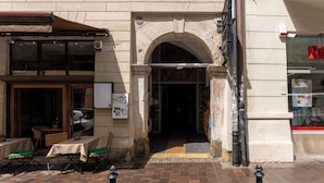 Ein Straßencafé mit Tischen, Stühlen und einer überdachten Sitzgelegenheit. Ein Geschäft mit einer Schaufensterschild.