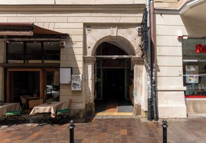 Ein Straßencafé mit Tischen, Stühlen und einer überdachten Sitzgelegenheit. Ein Geschäft mit einer Schaufensterschild.