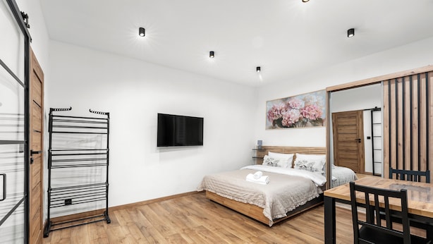 Ein Schlafzimmer mit Bett, Fernseher, Gemälde, Holzboden und einem Essbereich mit Stühlen.