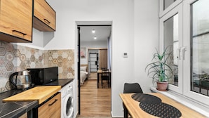 Eine kompakte Küche mit Mikrowelle, Wasserkocher und Waschmaschine. Es gibt einen Essbereich mit Tisch und Stühlen sowie einen Blumentopf am Fenster.
