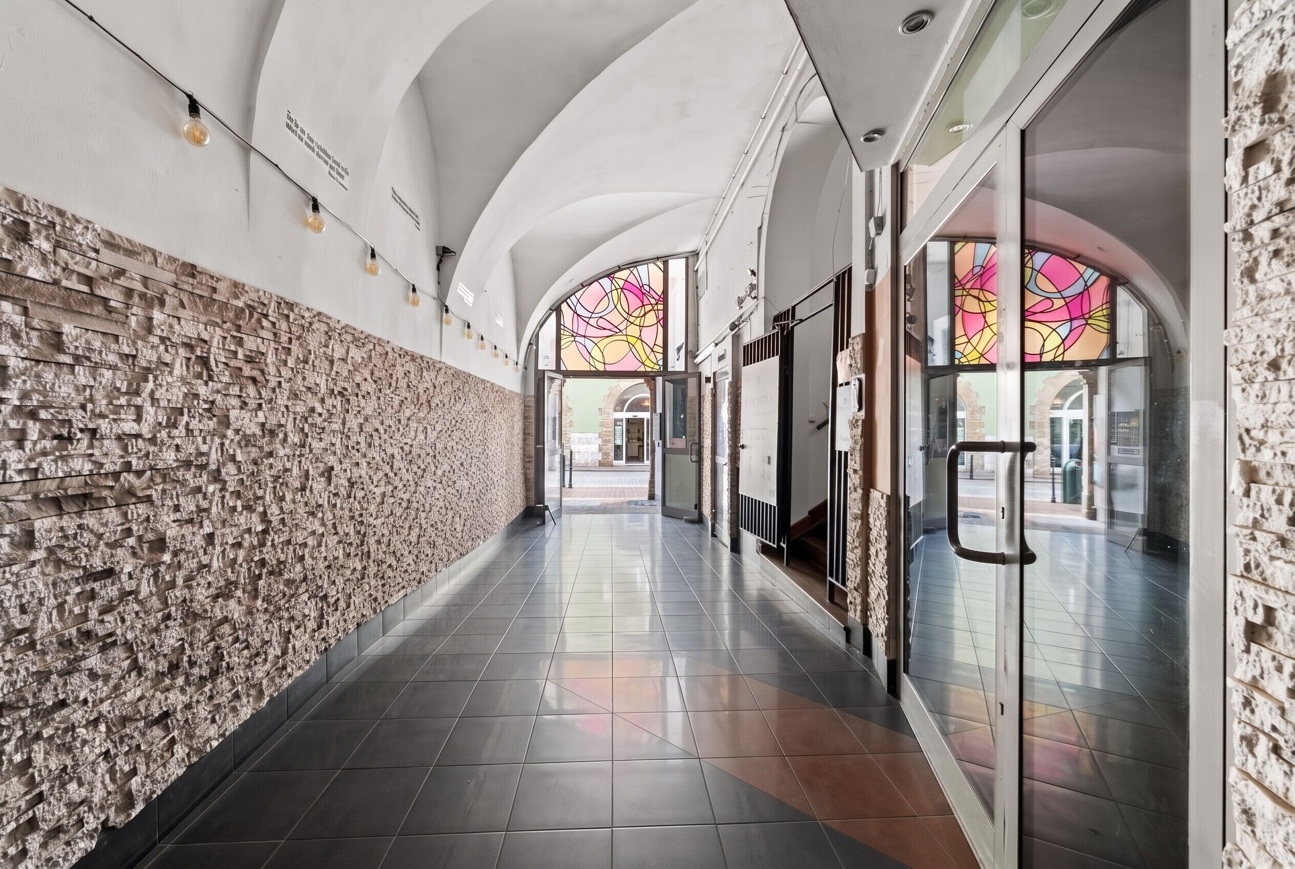 Un couloir avec un mur à motifs, des portes en verre et un sol carrelé.