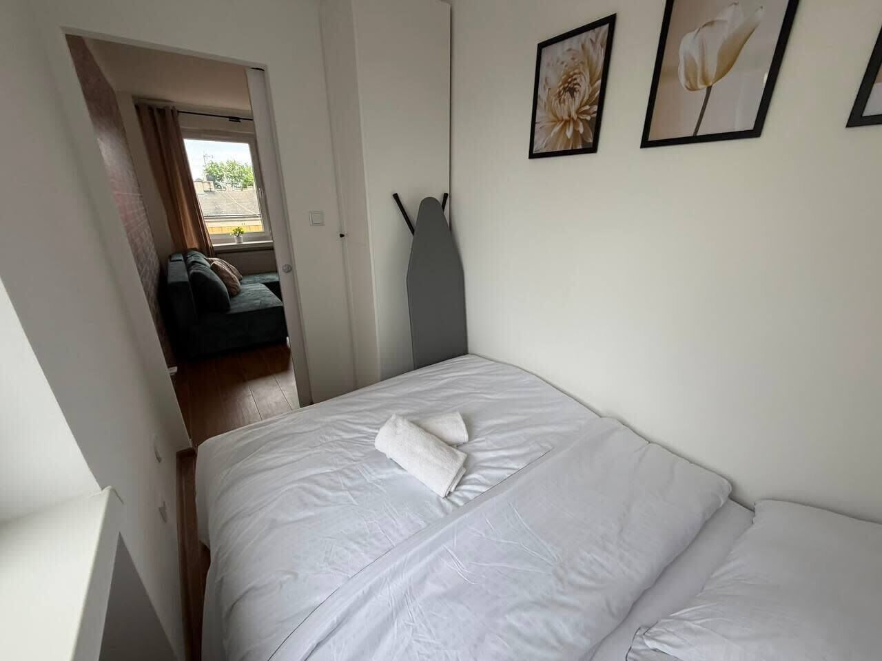 Um quarto com uma cama, uma porta que dá para outro cômodo e duas imagens emolduradas na parede.