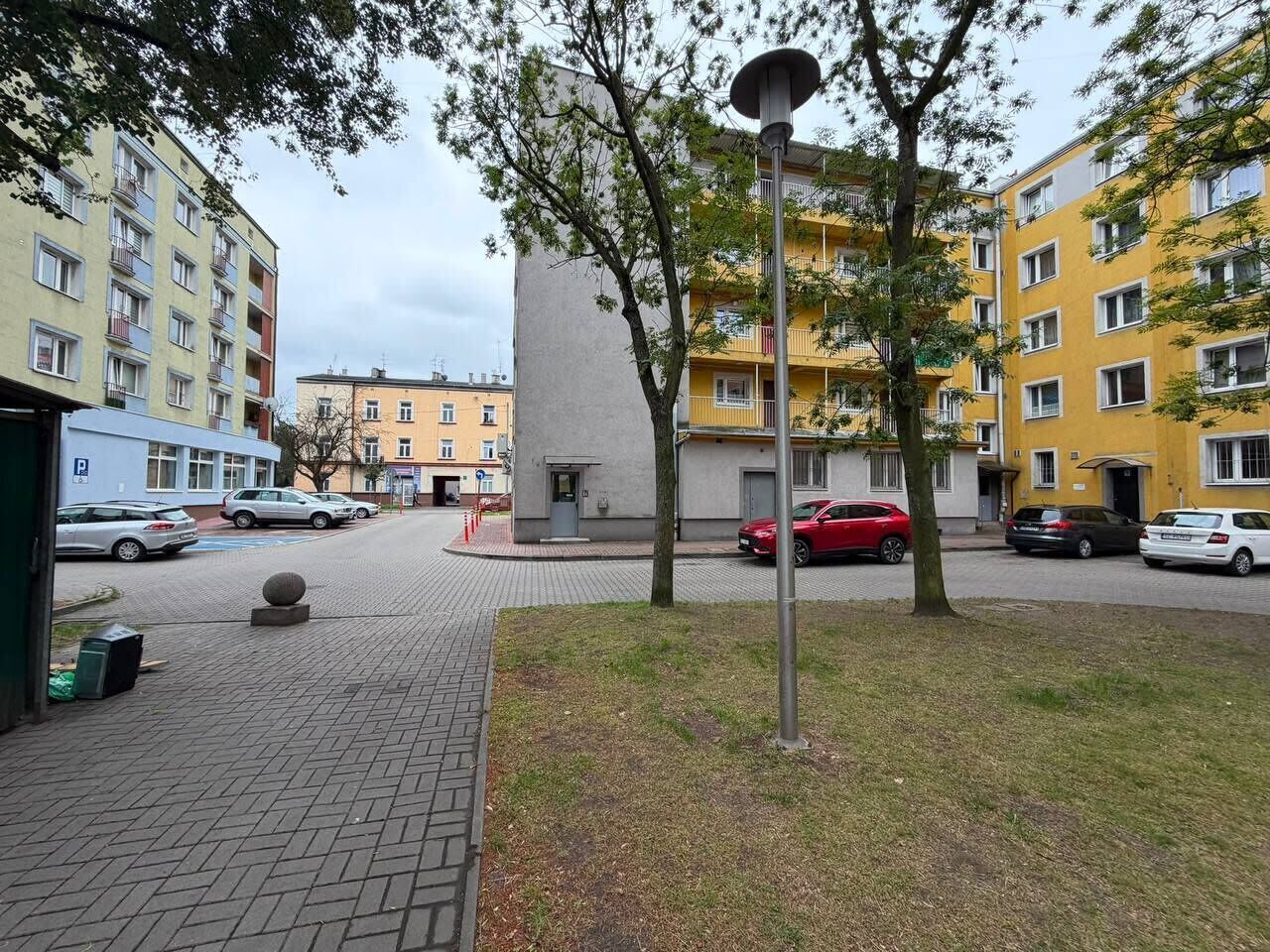 Uma área residencial com edifícios altos, um passeio pavimentado e carros estacionados.