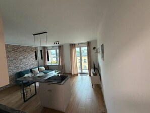A modern kitchen with a central island, a dining area with a sofa, and a large window with curtains.