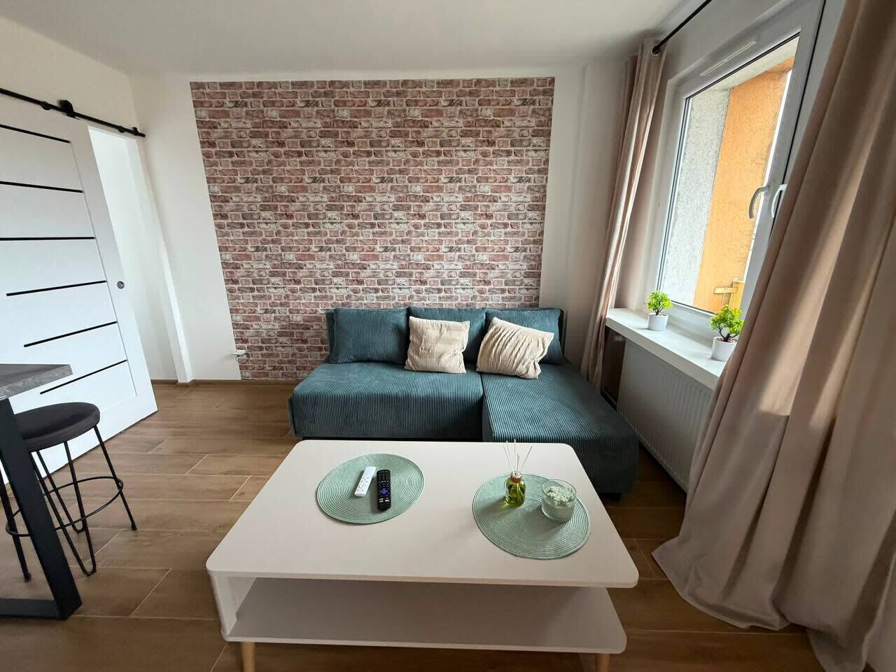 A compact living space with a brick-patterned wall, a sofa, a dining table, and a window with curtains.