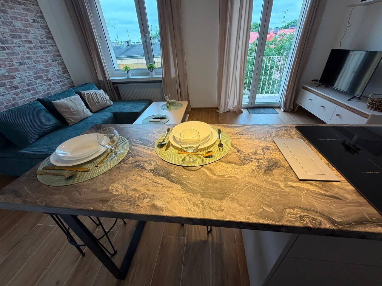 A dining area with a marble table, a sofa, and a TV in a modern apartment with large windows.